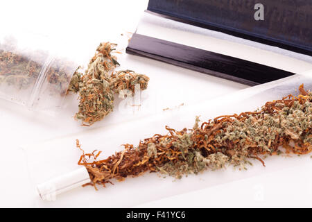 Close up Dried Cannabis Leaves on a Resealable Cellophane Wrapper and a Rolling Paper with Filter on Top of the Table Stock Photo