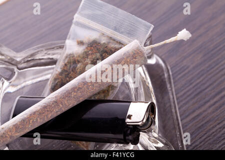 Close up of marijuana joint made with translucent rolling papers, plastic baggy of dried marijuana, black lighter and pipe on wh Stock Photo