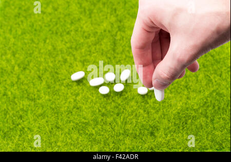 Male hand holding pill on background of tablets spilling  on the grass Stock Photo