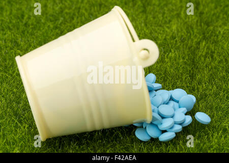 Blue pills spilled from a white bucket on the green grass background Stock Photo