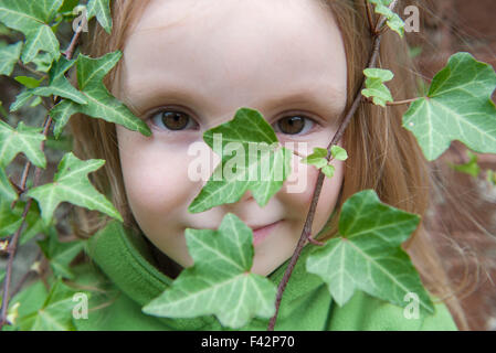 Little girl looking through ivy, close-up Stock Photo