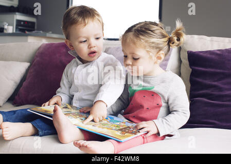 Young siblings looking at book together Stock Photo