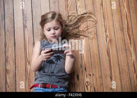 Little girl lying on floor using smartphone Stock Photo