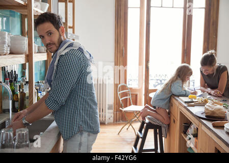 Family in kitchen, man doing dishes in foreground Stock Photo