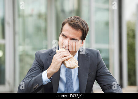 Businessman eating sandwich outdoors Stock Photo