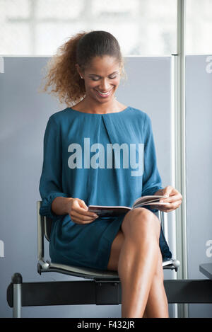 Woman reading in waiting room, smiling cheerfully Stock Photo