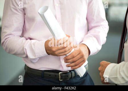 Businessman holding rolled up blueprint, talking with colleague, cropped Stock Photo