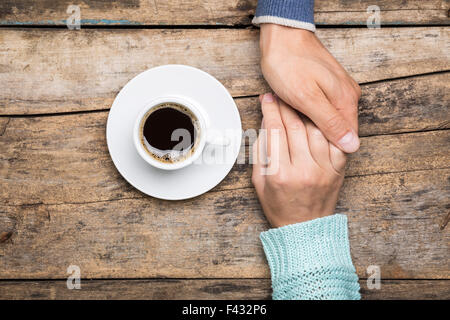 Man holds woman's hand with cup of coffee top view image on wooden backdrop. Friendship coffee background Stock Photo