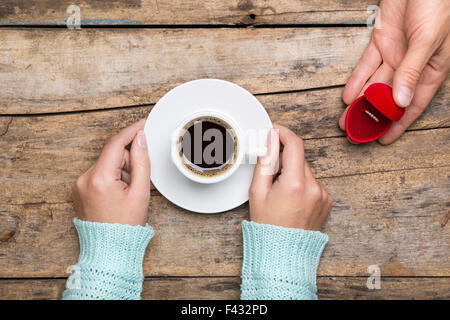 Woman holds cup of coffee and man gives gold ring as a gift for birthday or engagement Stock Photo