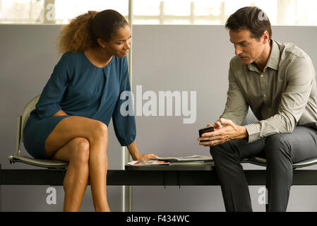 Professionals chatting in waiting room, man showing woman smartphone Stock Photo