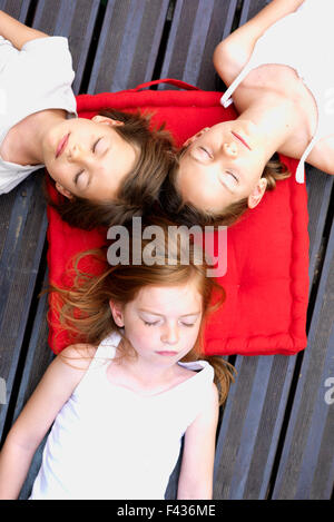 Girls napping outdoors with heads resting on shared cushion Stock Photo