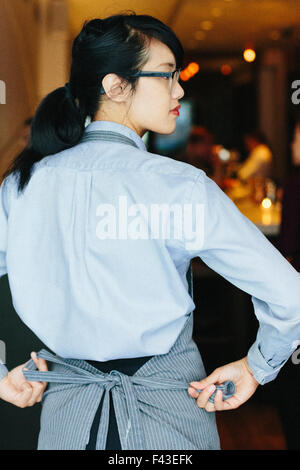 Young waitress tying her apron at a city restaurant. Stock Photo