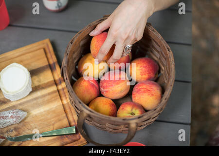 View from overhead of a picnic table with a basket of fresh peaches and a cheese board. Stock Photo
