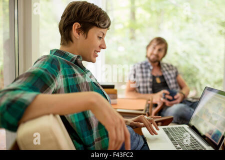 A woman sitting using a laptop, and a man seated in a chair on the terrace. Stock Photo