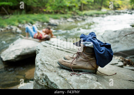 A young man and woman on the rocks on a river bank. Jeans and boots on a rock. Stock Photo