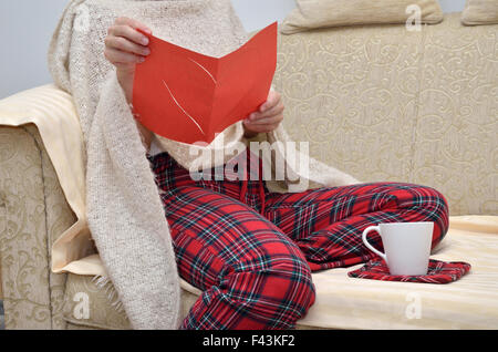 Lady in cozy home wear sitting on sofa and reading a love letter Stock Photo