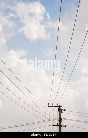 Power transmission lines from a transmission pole run across a blue sky being covered with fast approaching grey rain clouds. Stock Photo