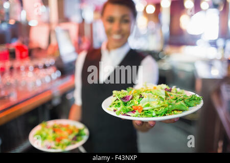 Pretty barmaid holding plates of salads Stock Photo