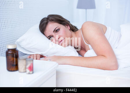 Sad woman looking at pills in bed Stock Photo