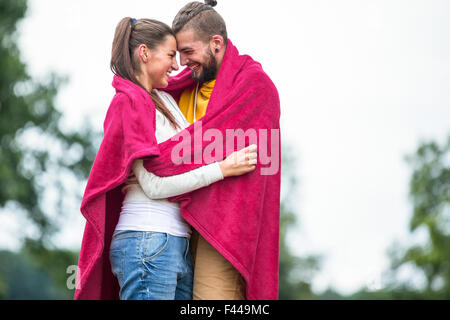 Happy couple hugging under blanket Stock Photo