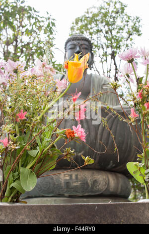 Metal Buddha statue meditation pose behind flowers giant lotus base Stock Photo