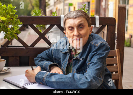 Adult disabled man with cerebral palsy sitting with a notebook at an outdoor cafe. Stock Photo