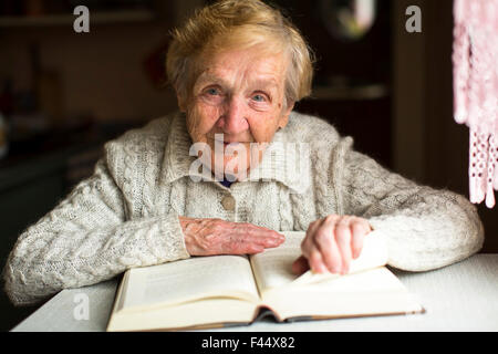An old woman sitting with a book at the table. Stock Photo