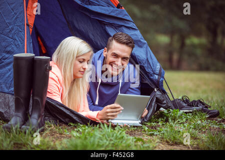 Happy couple lying in their tent using tablet Stock Photo