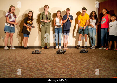 Excited multiracial preteens and a librarian watch a 'Robot Challenge Night' race at a public library multipurpose room in Laguna Niguel, CA. The remote control robots are assembled from a selection of snap-on spare parts. Stock Photo