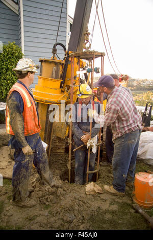 A soil technician in a "safety cage" is lowered down a narrow vertical hole drilled by the core cutter (left) to inspect the soil layers beneath a hillside home undermined by flooding from heavy rains in Laguna Niguel, CA. Stock Photo