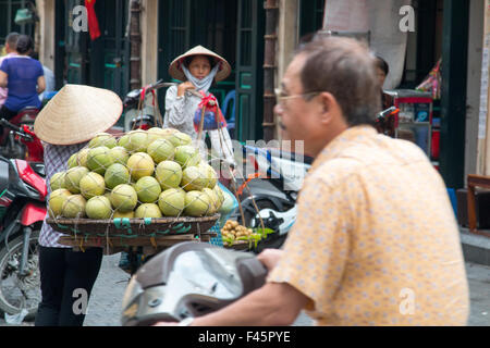 Vietnam,Hanoi Old Quarter, mature man on scotter rides past two ladies selling fruit on the streets of Hanoi,Vietnam. Stock Photo