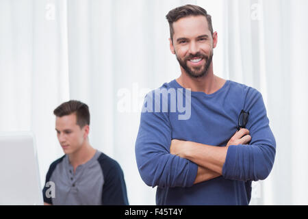 Happy casual businessman looking at camera with arms crossed with his colleagues behind Stock Photo