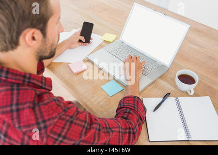 Creative businessman typing on laptop and using smartphone at desk Stock Photo