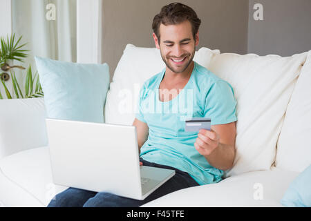 Happy handsome man sitting on couch shopping online with laptop Stock Photo