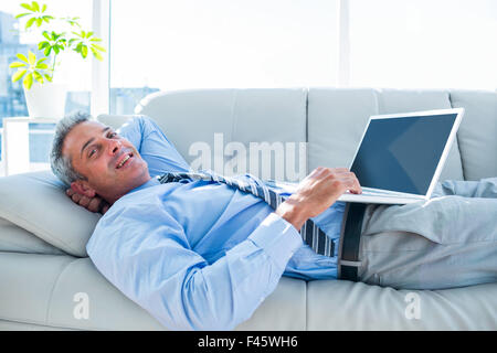 Happy businessman relaxing on a couch and using laptop computer Stock Photo