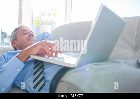 Happy businessman relaxing on a couch and using laptop computer Stock Photo