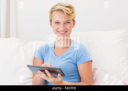 Portrait of smiling woman sitting on couch and using tablet computer Stock Photo