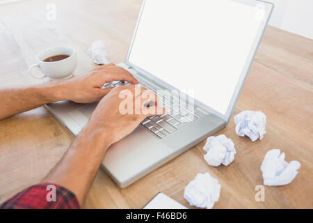 Hands typing on a laptop with paper pellets beside Stock Photo