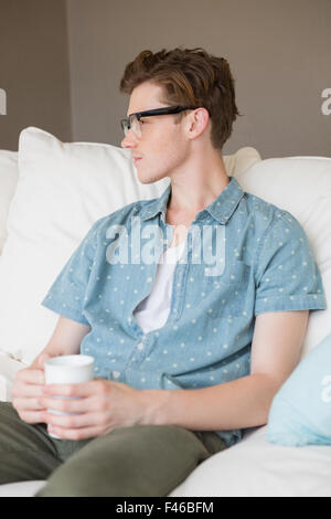 Thoughtful young man sitting on couch with a mug Stock Photo