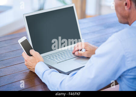 Businessman working on laptop computer and holding smartphone Stock Photo