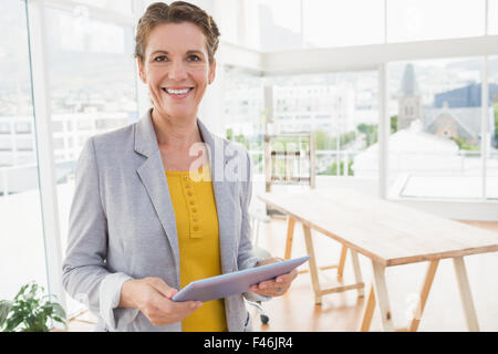 Creative businesswoman smiling at camera and holding tablet Stock Photo