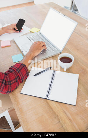Man typing on laptop and using smartphone at desk Stock Photo