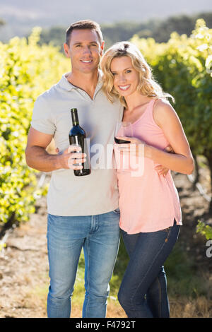 Smiling couple holding wine and standing in front of grapevine Stock Photo