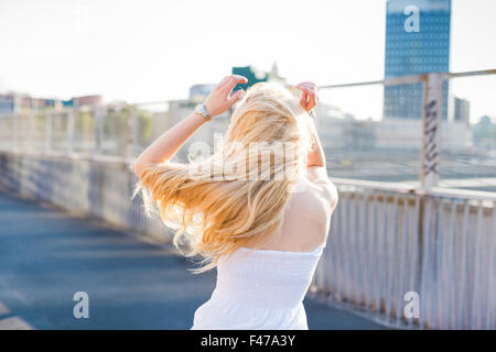 young handsome caucasian long blonde straight hair woman dancing in the city, view from back, feeling free in the city - dancing, freedom, youth concept Stock Photo