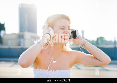 Half length portrait of young handsome caucasian long blonde straight hair woman listening music with headphones and smartphone Stock Photo