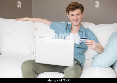 Happy young man sitting on sofa shopping online with laptop Stock Photo