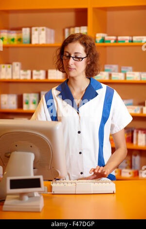Pharmacist typing on computer behind pharmacy counter Stock Photo