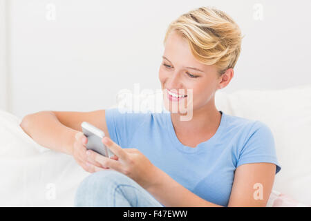 Smiling woman sitting on couch and using smartphone Stock Photo