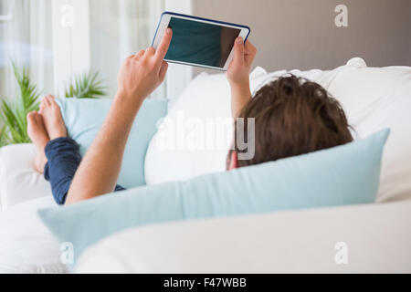 Rear view of man lying on couch using tablet Stock Photo