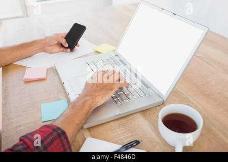 Man typing on laptop and using smartphone at desk Stock Photo